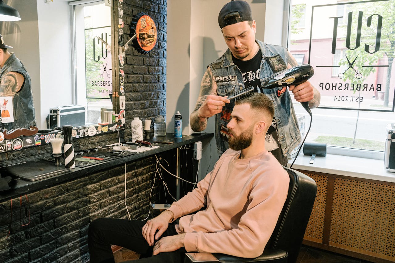 Barber styling a man's hair with a blow dryer in a contemporary barbershop setting.